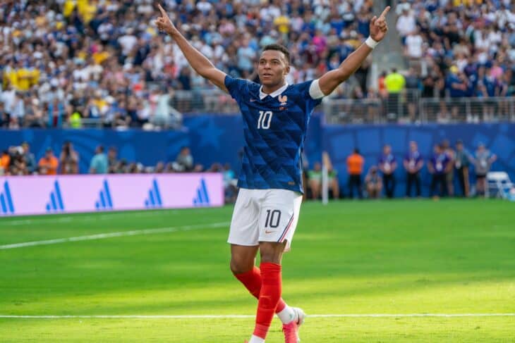 Kylian Mbappé in France's number 10 shirt with arms raised, celebrating in front of the crowd