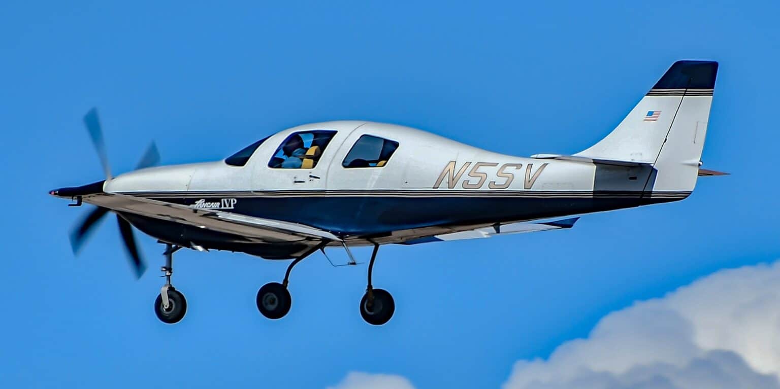White and navy Lancair IV-P N5SV in flight with its landing gear extended against a blue sky