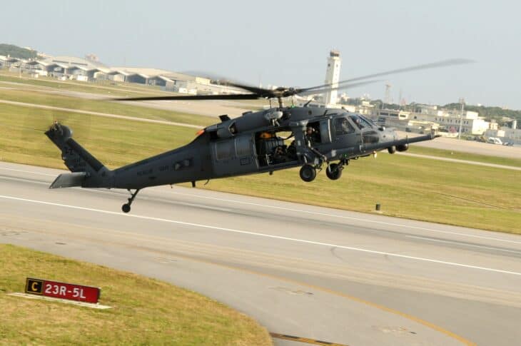 HH-60 Pave Hawk rescue helicopter coming in to land on Okinawa with an airfield tower behind it