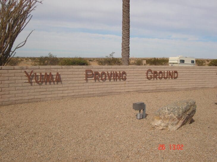 Brick wall sign reading Yuma Proving Ground beside the desert road