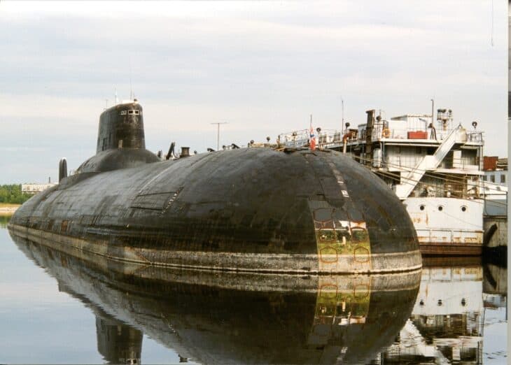 Typhoon-class submarine moored at a Russian shipyard, its rounded hull reflected in the water