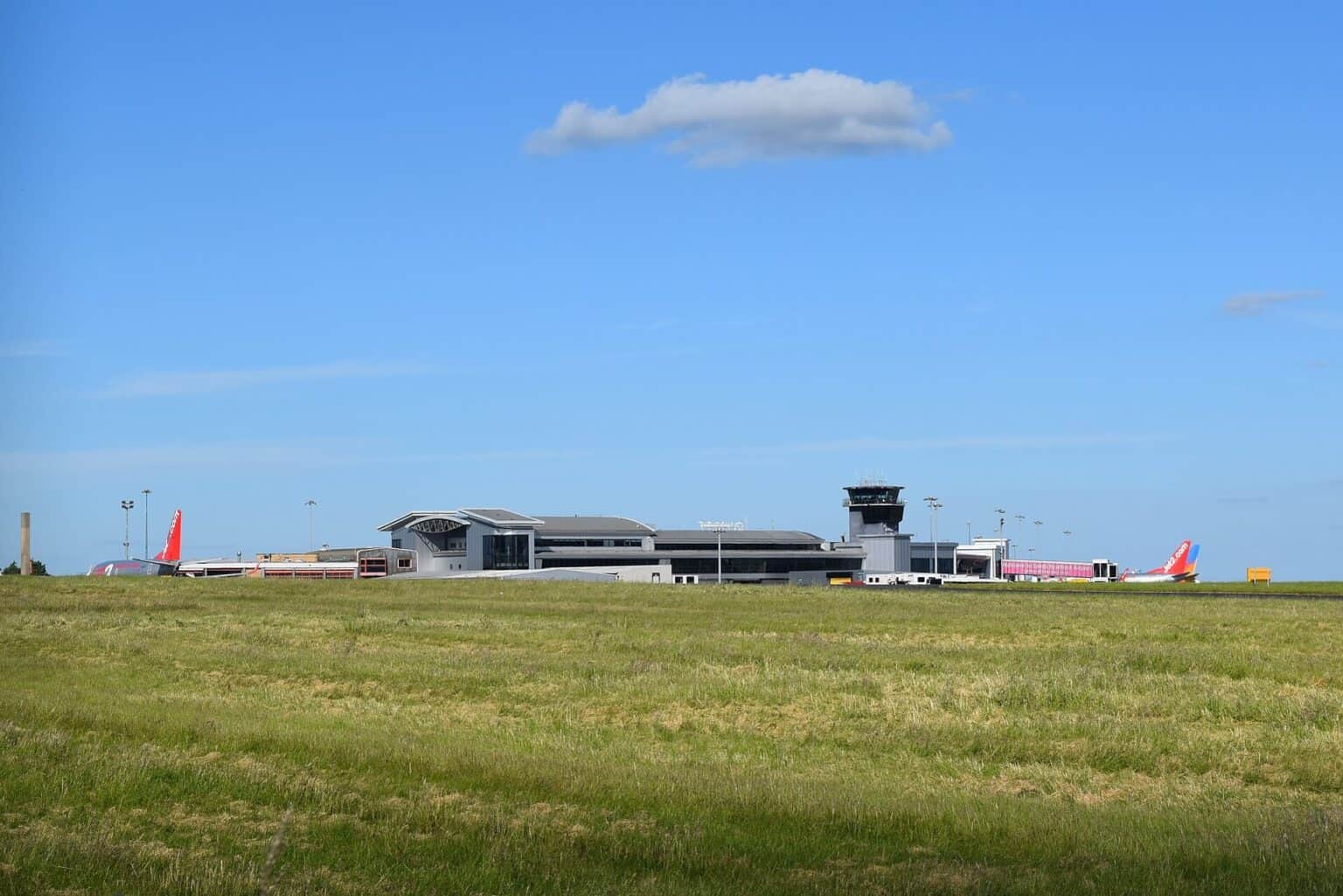 Leeds Bradford Airport terminal and air traffic control tower seen across the airfield grass, with airliners parked on the apron