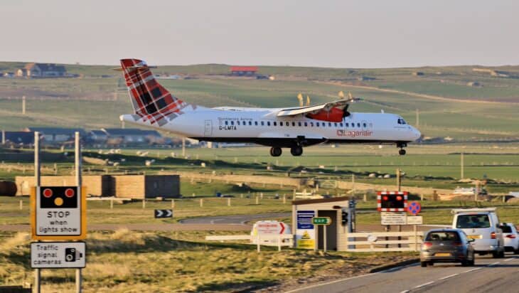 Loganair ATR 72-600 G-LMTA on final approach to Sumburgh Airport, low over a road with traffic lights and waiting cars