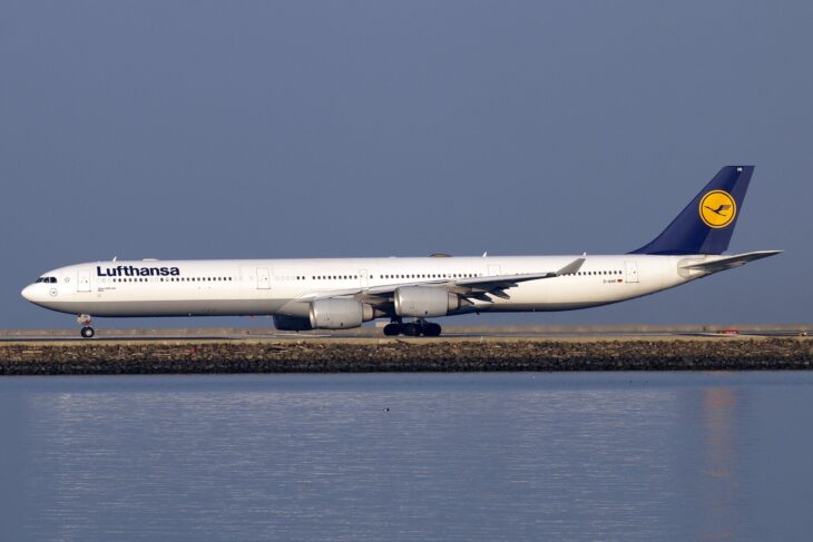 Lufthansa Airbus A340-600 D-AIHK on the runway at San Francisco International Airport in full side profile, all four engines visible, with San Francisco Bay in the foreground