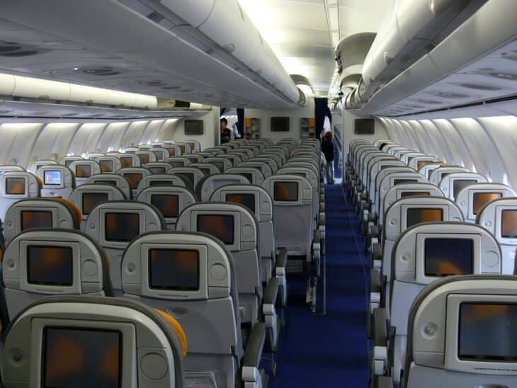 Economy cabin of Lufthansa Airbus A340-600 D-AIHK, rows of grey seats with seatback screens either side of a blue-carpeted aisle