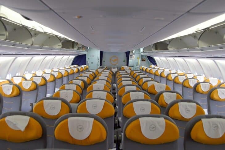 Rear economy cabin of Lufthansa Airbus A340-600 D-AIHB with new yellow and grey seats and the Lufthansa crane logo on the bulkhead