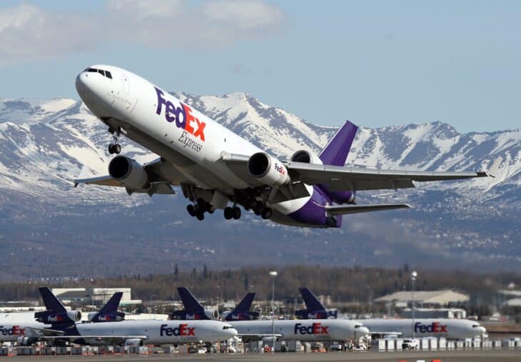 FedEx MD-11F climbing out of Anchorage with a row of parked FedEx MD-11 tails below