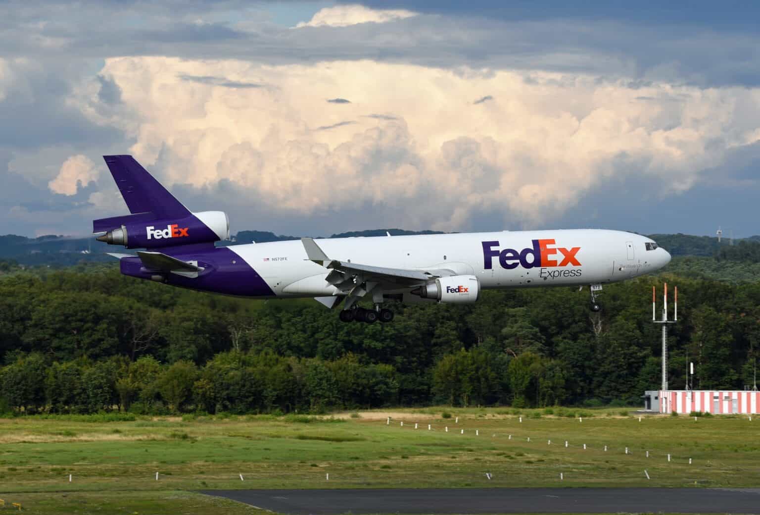 FedEx Express McDonnell Douglas MD-11F on short final with its landing gear down, three engines visible, under towering clouds