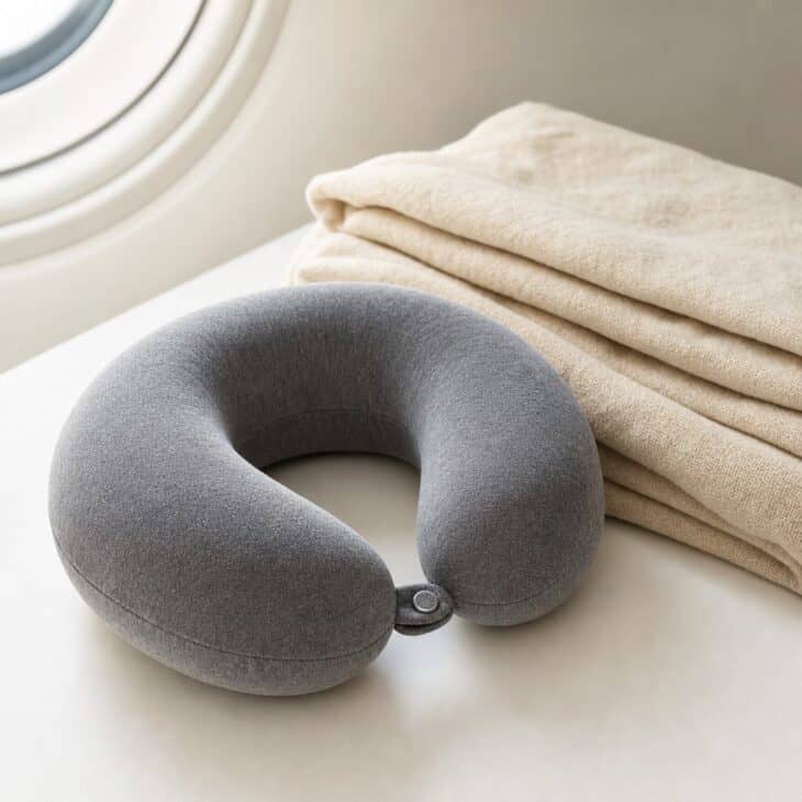 Grey memory foam neck pillow beside a folded blanket
