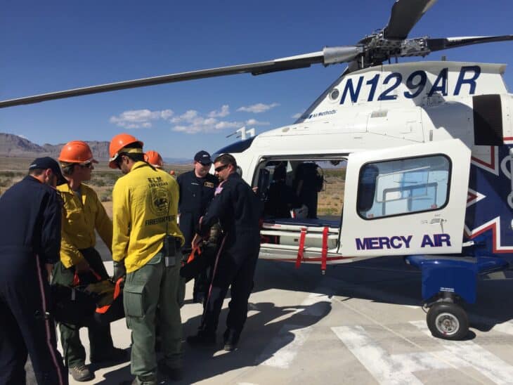 Wildland firefighters load a stretcher into Mercy Air helicopter N129AR on a sunny helipad