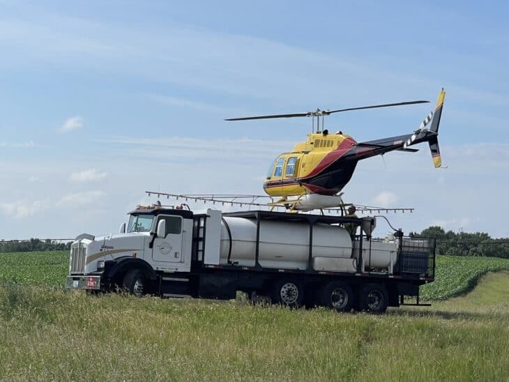 Black and yellow Bell 206 crop-spraying helicopter parked on a landing pad atop its refueling truck in a field