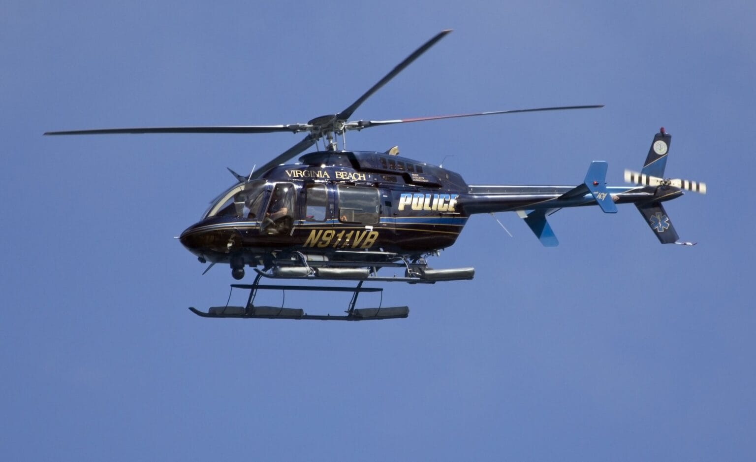 Black Bell 407 police helicopter N811VB in flight against a blue sky