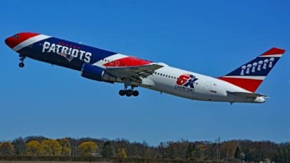 Patriots-liveried Boeing 767 N36NE climbing steeply after takeoff against a blue sky