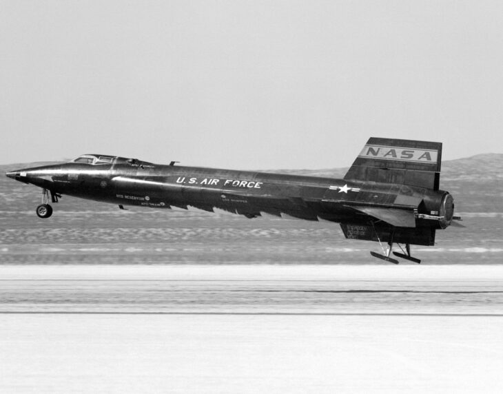 Black North American X-15 landing on a dry lakebed with skids touching down