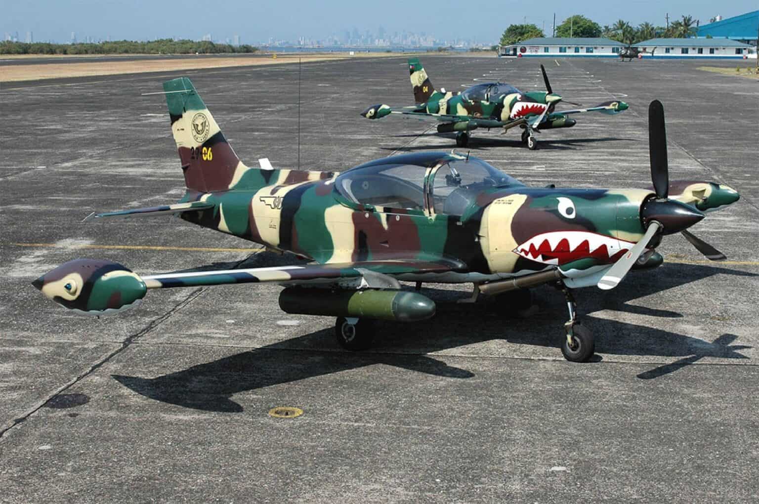 Two camouflaged Philippine Air Force SF-260 trainers with shark-mouth nose art parked on a ramp