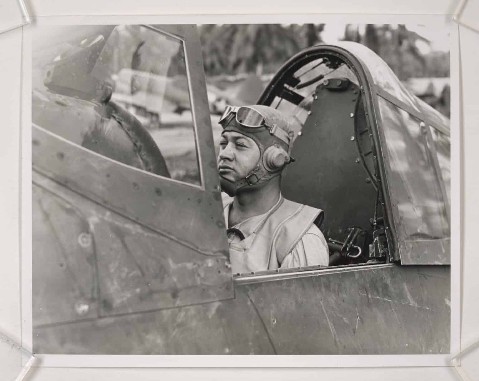 Marine Corps fighter pilot Gregory Boyington sitting in the cockpit of a Corsair in goggles and helmet