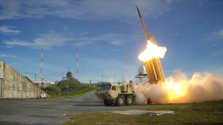 THAAD interceptor climbing away from its truck-mounted launcher on a test range, with fire and smoke at the base