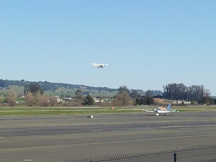 Light airplane climbing away from the runway at Petaluma Municipal Airport with hills in the background