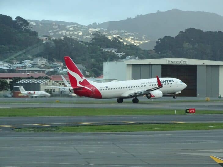 Qantas Boeing 737-800 VH-XZG on a runway with a hangar and hillside houses behind
