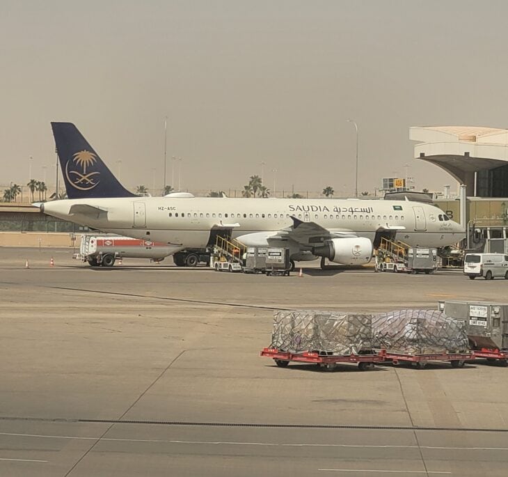Saudia Airbus A320 HZ-ASC parked on the apron at King Khalid International Airport in Riyadh with baggage carts nearby