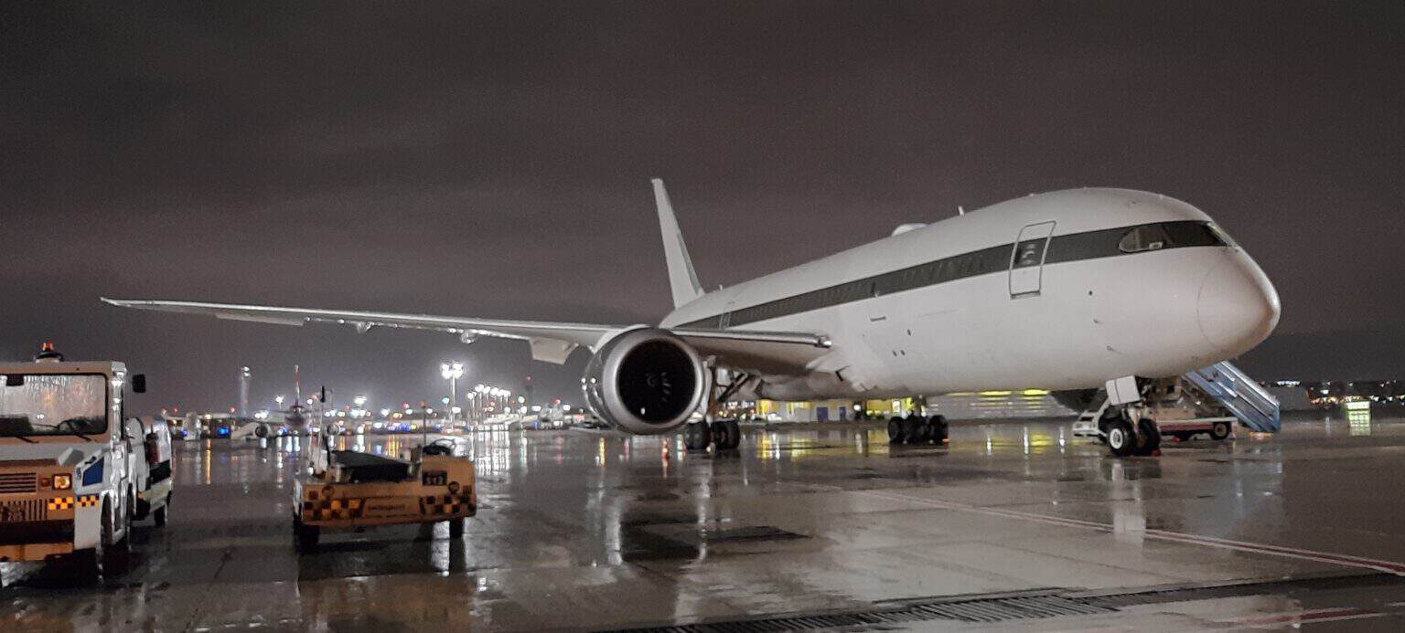 Boeing 787-8 Dreamliner P4-BDL parked on a wet apron at night with boarding stairs at the front door