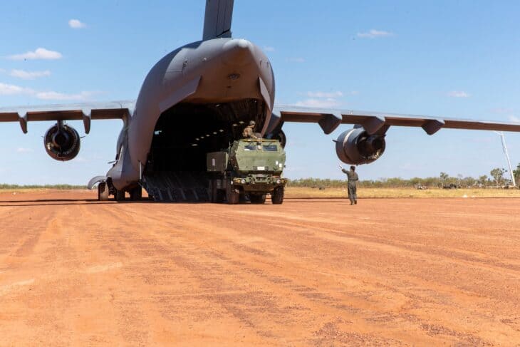 HIMARS rocket launcher driving out of the rear ramp of a RAAF C-17A on a red dirt strip