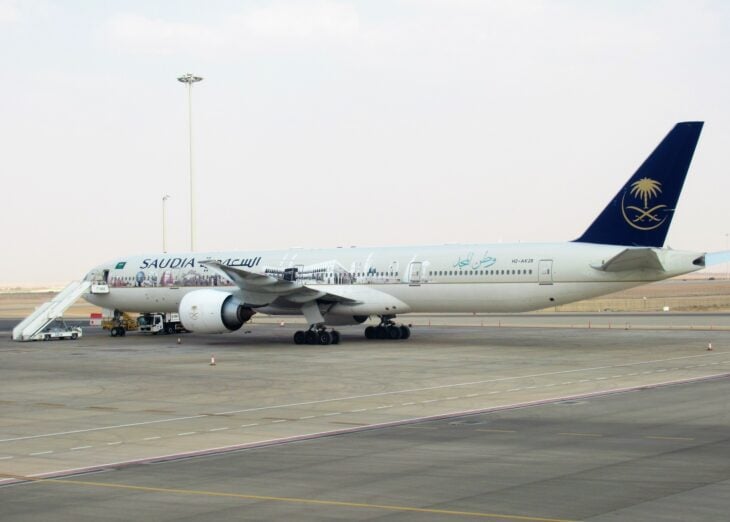 Saudia Boeing 777-300ER HZ-AK28 parked on a remote stand at King Khalid International Airport with boarding stairs attached
