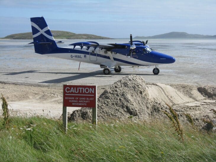 Scottish Loganair Twin Otter on the sand of Barra's beach runway beside a caution sign