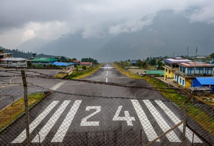 The threshold of runway 24 at Lukla with the strip climbing toward the village and the Himalayan foothills