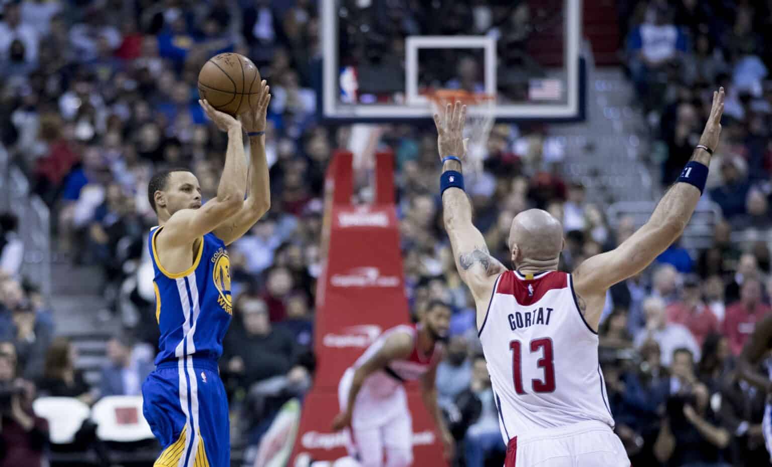 Stephen Curry of the Golden State Warriors rising for a jump shot over a defender with the arena crowd behind him