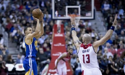Stephen Curry of the Golden State Warriors rising for a jump shot over a defender with the arena crowd behind him