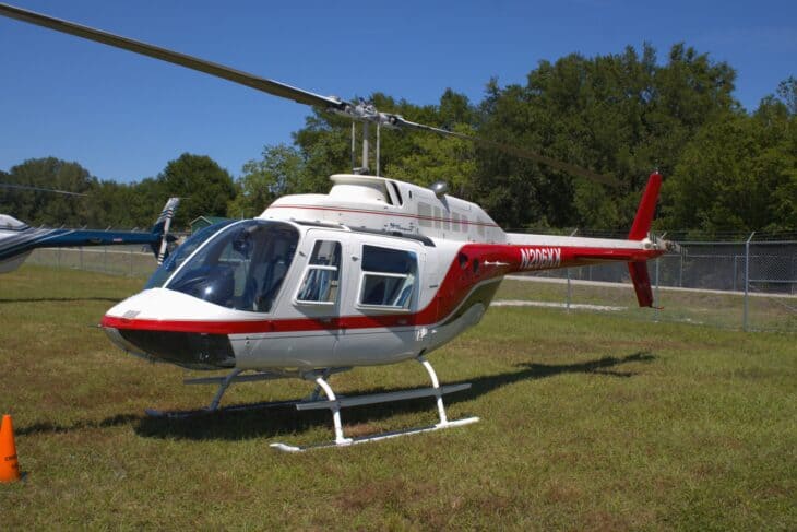 White and red Bell 206B-3 JetRanger III sitting on grass at an airfield