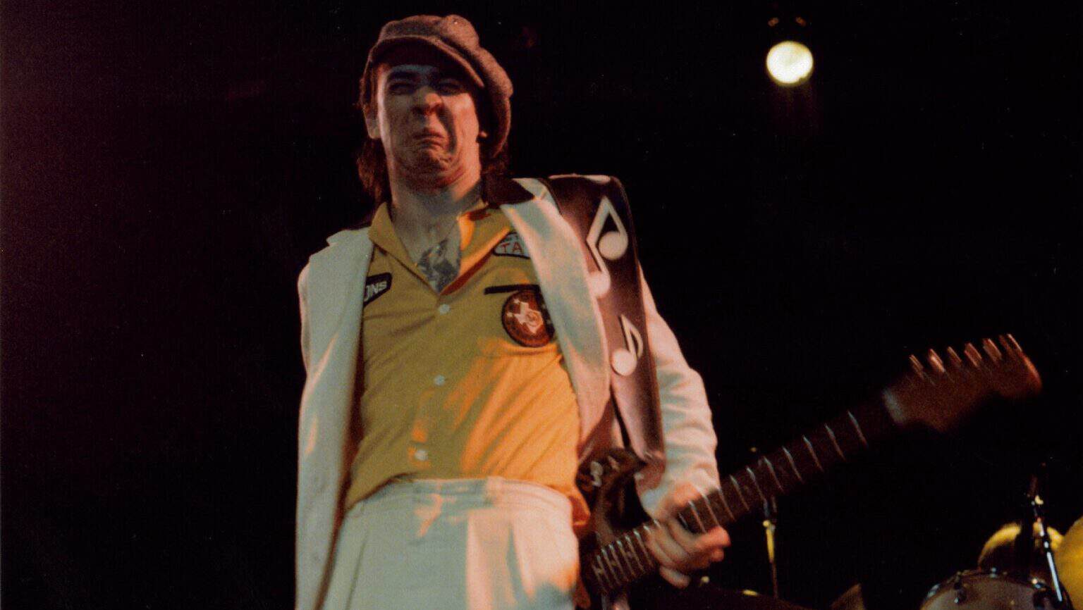 Stevie Ray Vaughan on stage in a yellow shirt and white suit, playing a Stratocaster at the Ritz Theater