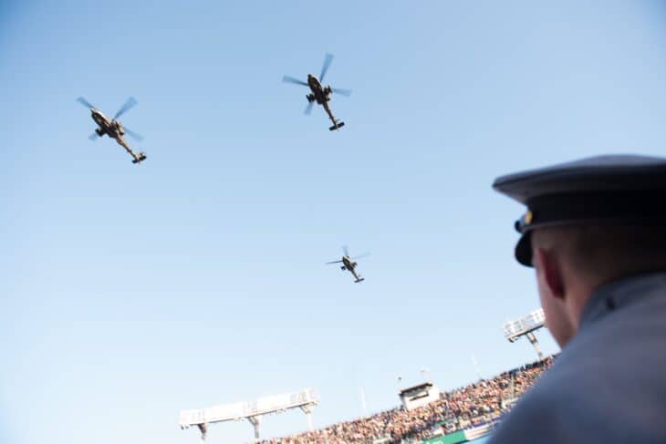 Three AH-64 Apache helicopters flying over a packed football stadium
