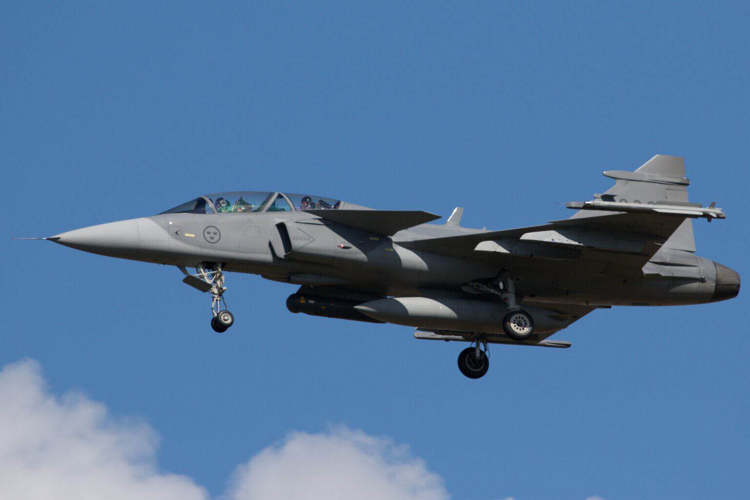 Swedish Air Force Saab JAS 39D Gripen with landing gear down against a blue sky with clouds