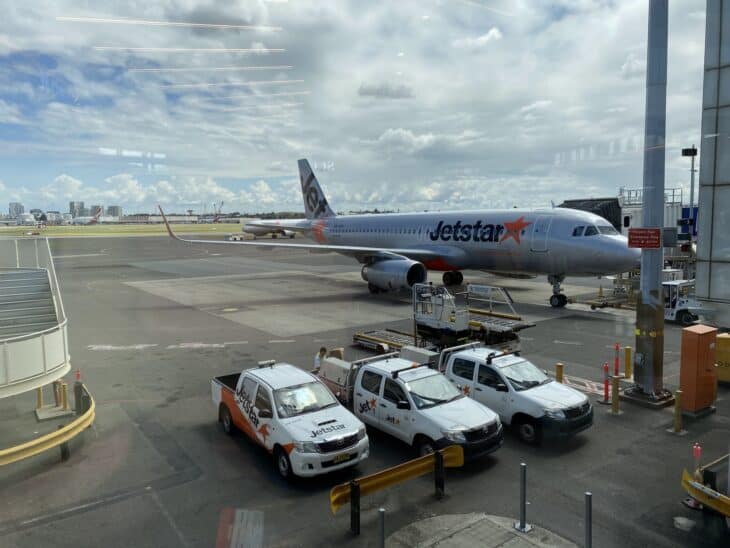 Jetstar Airbus A320 parked at a Sydney Airport gate with baggage trucks on the apron