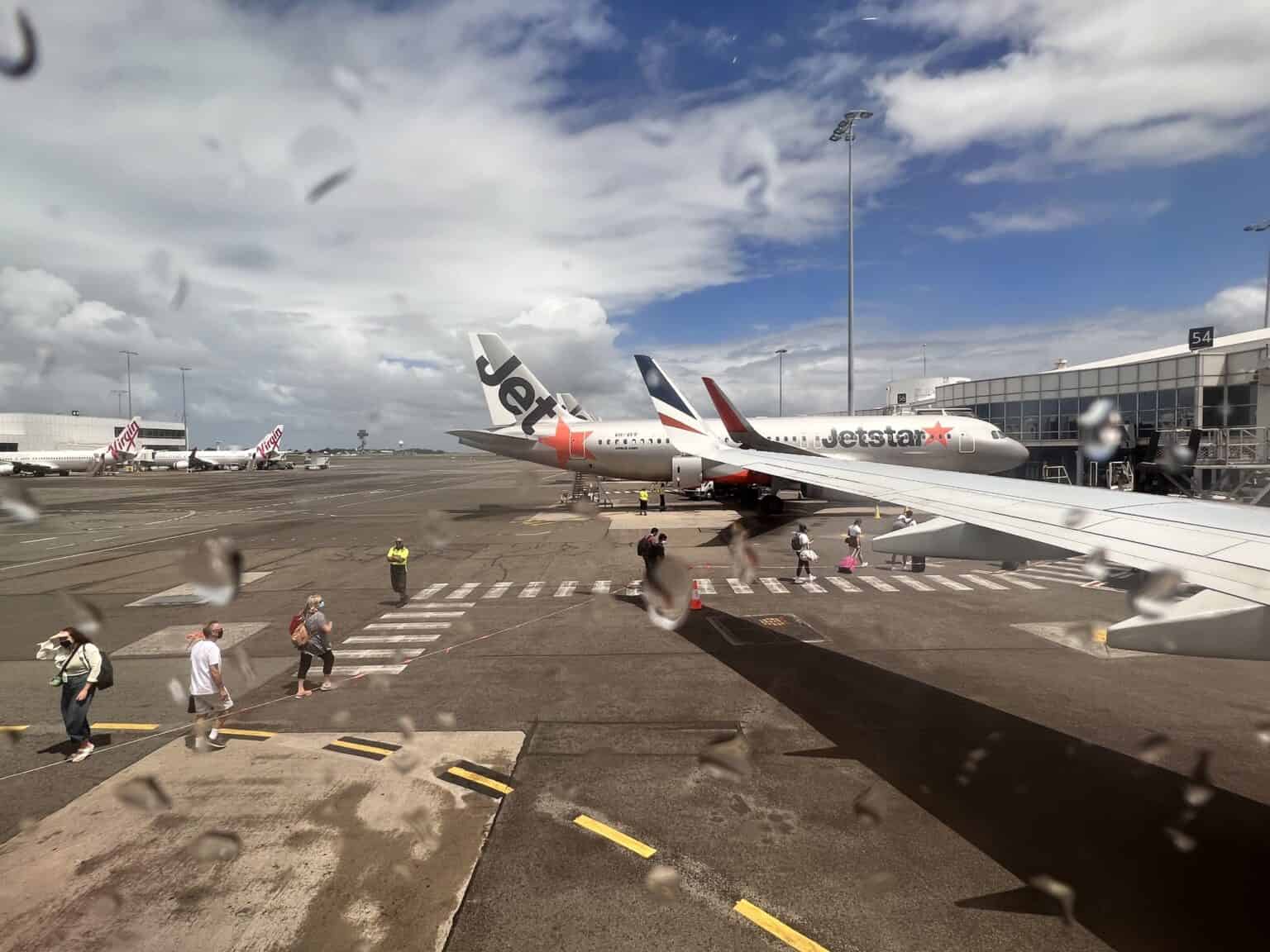 Jetstar and Virgin Australia jets parked at Sydney Airport's domestic Terminal 2 under a cloudy sky