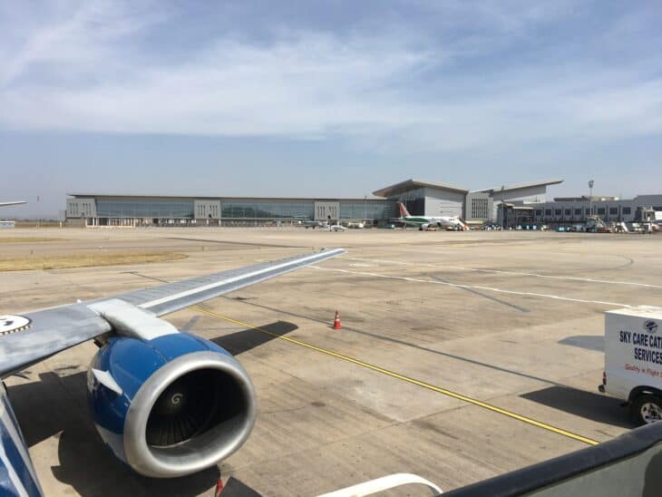 Apron and terminal buildings at Abuja's Nnamdi Azikiwe International Airport, seen past an airliner's wing and engine