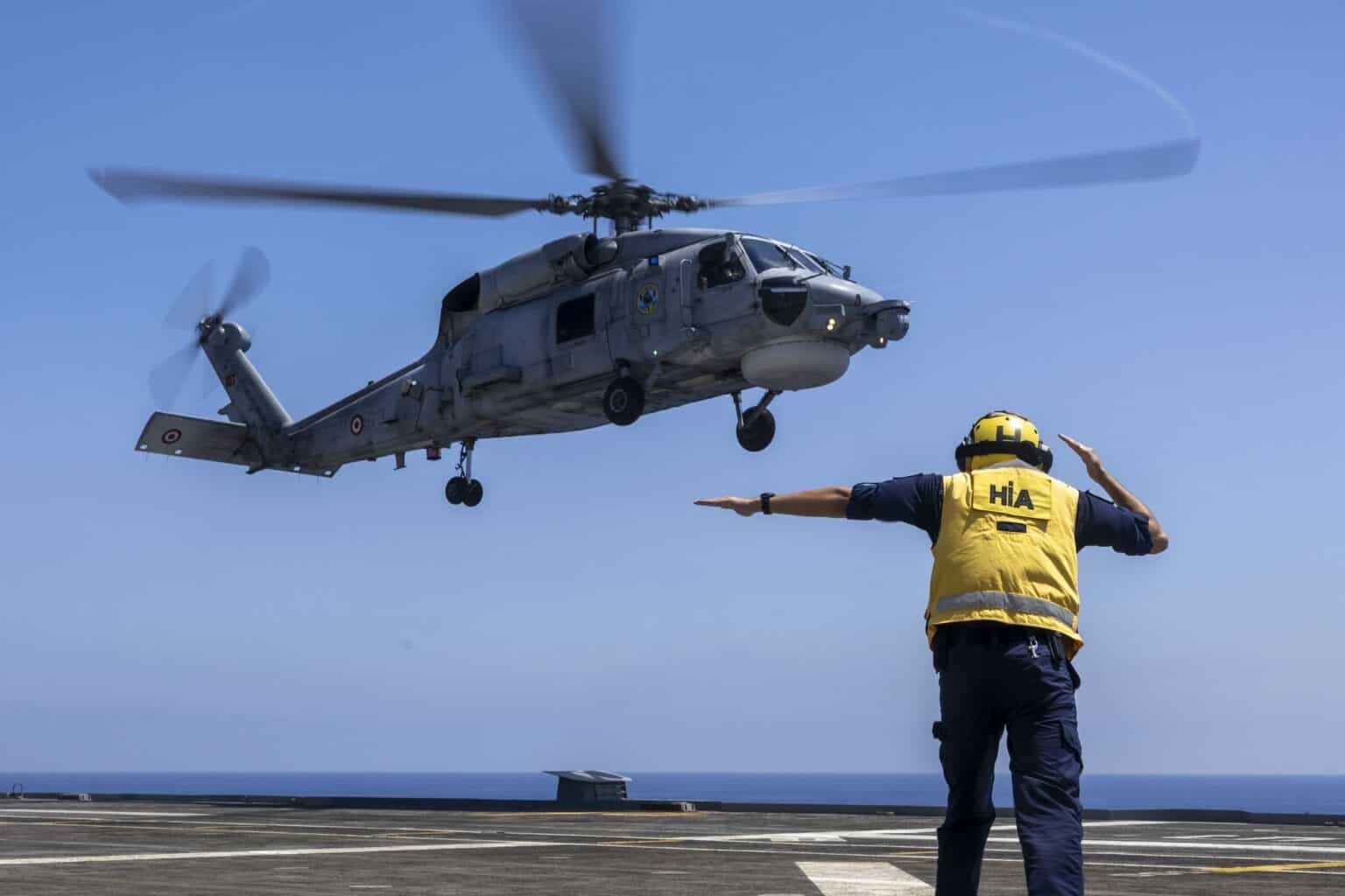 Turkish SH-70 Sea Hawk helicopter landing on the flight deck of TCG Anadolu as a deck crewman signals