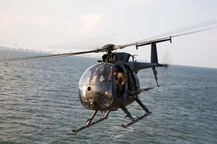 MH-6 Little Bird skimming low over water with operators on the skids
