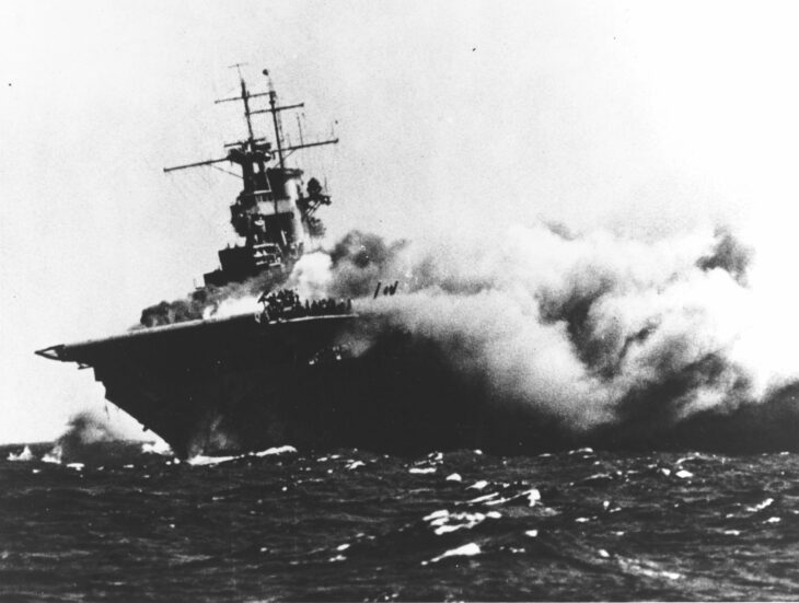 USS Wasp (CV-7) with smoke and fire pouring from her bow after torpedo hits