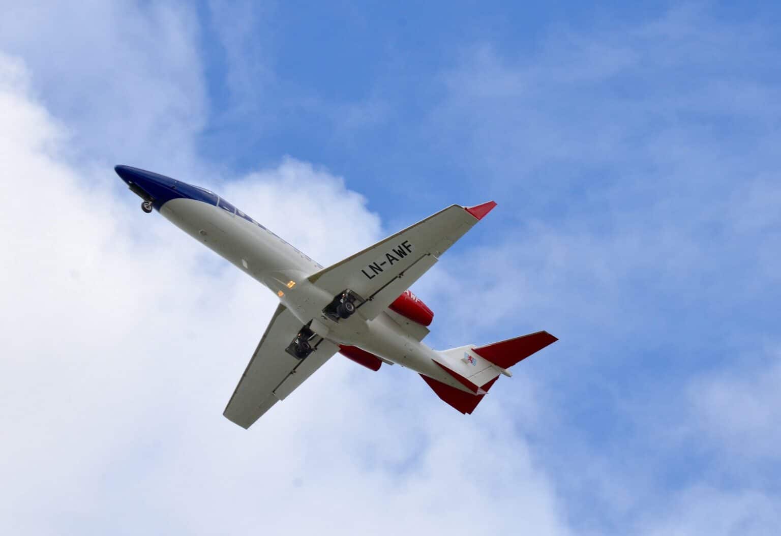 Bombardier Learjet 45 climbing against a blue sky with scattered cloud, seen from below