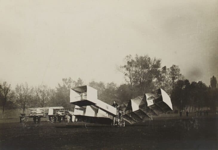 Santos-Dumont 14-bis biplane with its box-kite wing cells, standing on a grass field in 1906