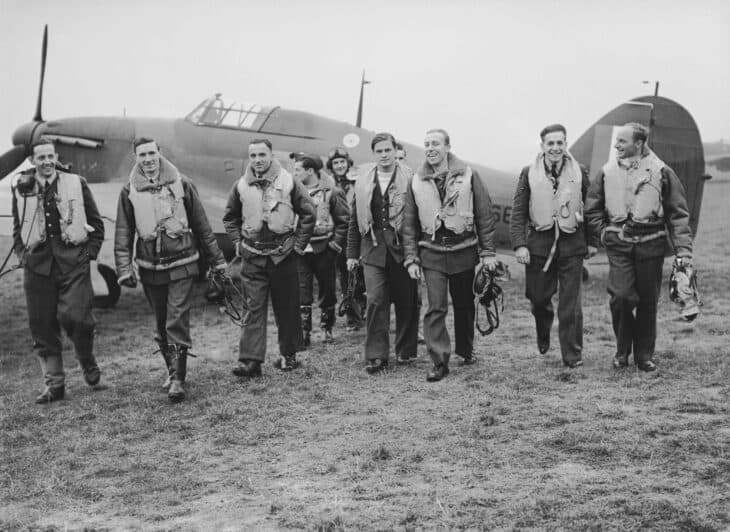 Pilots of No. 303 Polish Squadron walking in flying gear past a Hurricane